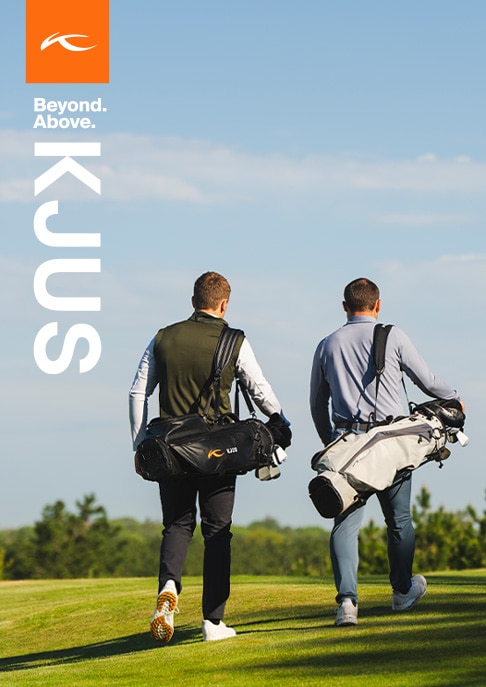 Two golfers wearing KJUS apparel walk astride on a sunny fairway, making conversation on the way to their next shot.