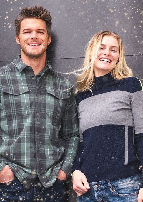 A man and woman smiling against a grey background with sparkles around them wearing KJUS clothing.