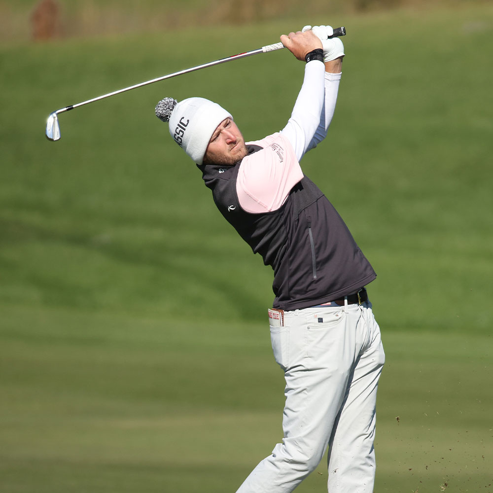 KJUS athlete Lee Hodges wearing a beanie and vest swings a golf club.