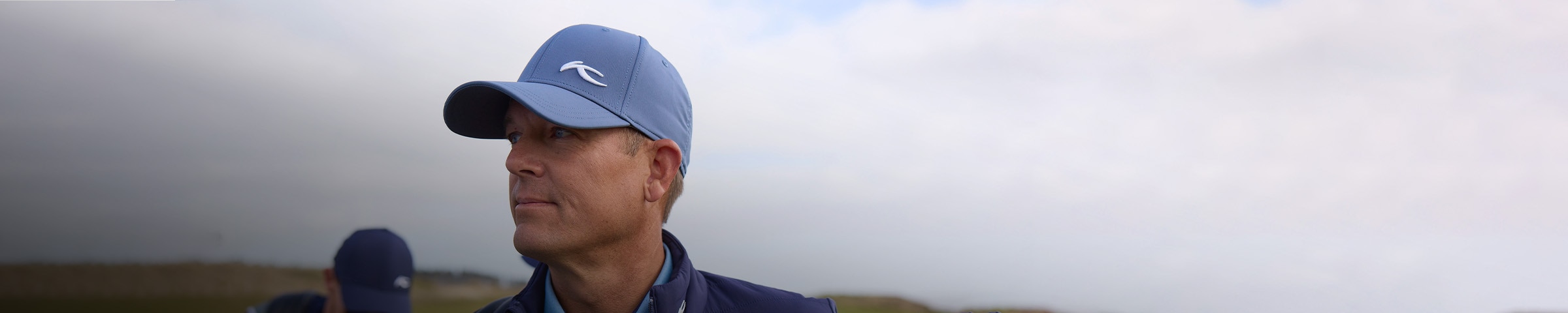 A man wearing a KJUS cap looks out over a golf course.