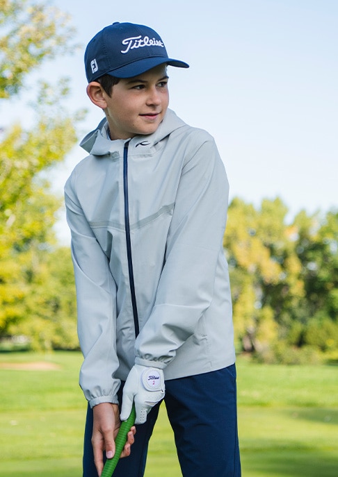 A junior golfer wearing a KJUS rain jacket prepares to putt at the green.